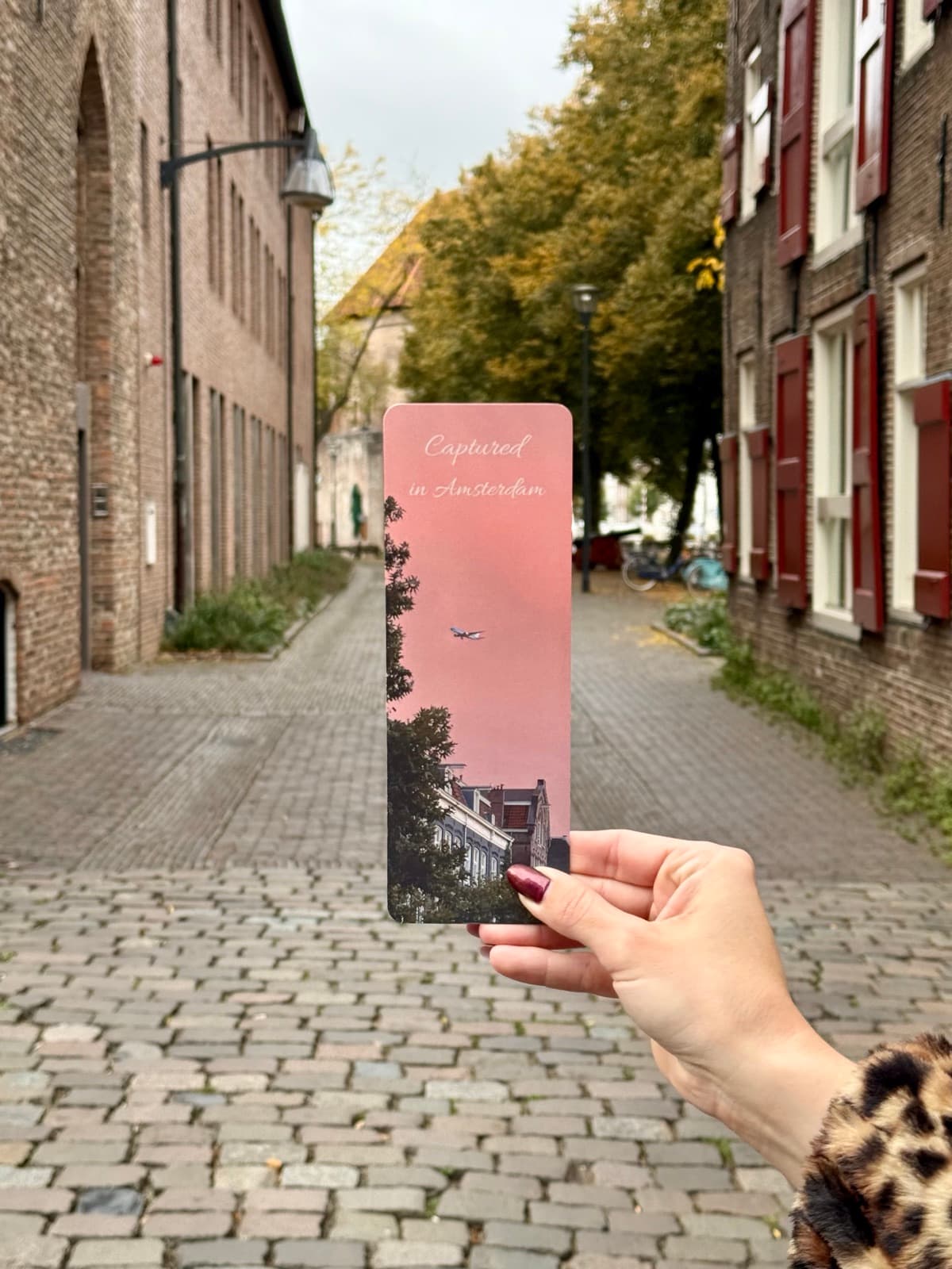 The Amsterdam pink-sky bookmark held up in a quiet Amsterdam street